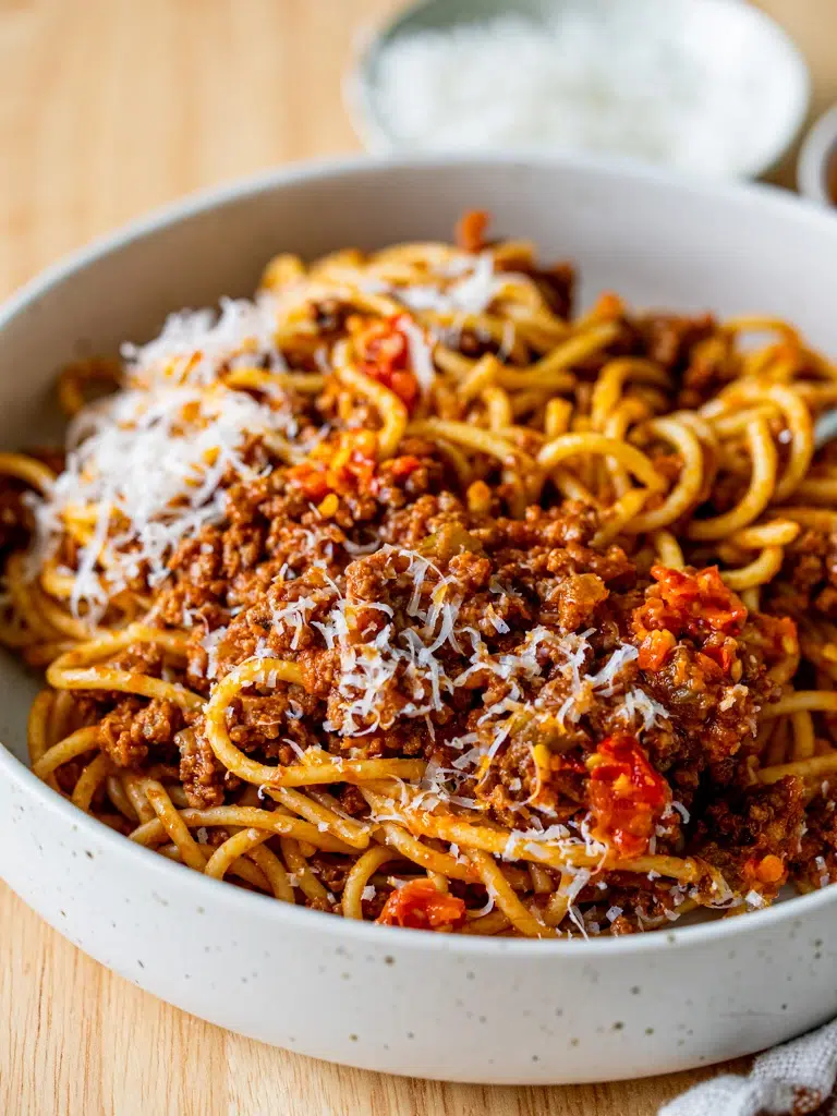 Side view of Bolognese sauce with pasta with grated cheese and red chilli served on a small saucer on the side.