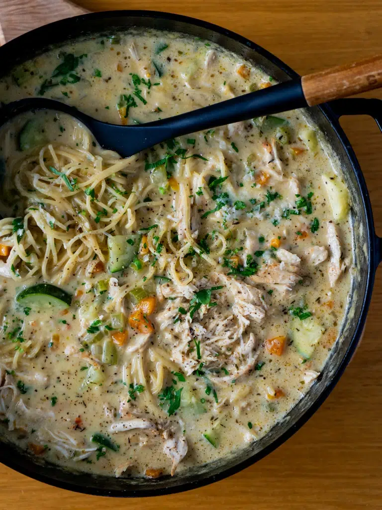 Overhead view of a pan filled with creamy lemon chicken noodle soup, garnished with fresh herbs.