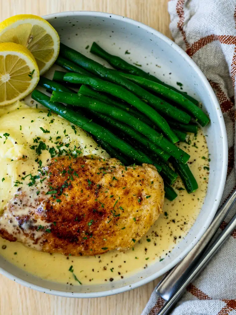 Top view of a plated Creamy Lemon Pepper Chicken served with green beans, mashed potatoes, and a rich sauce.