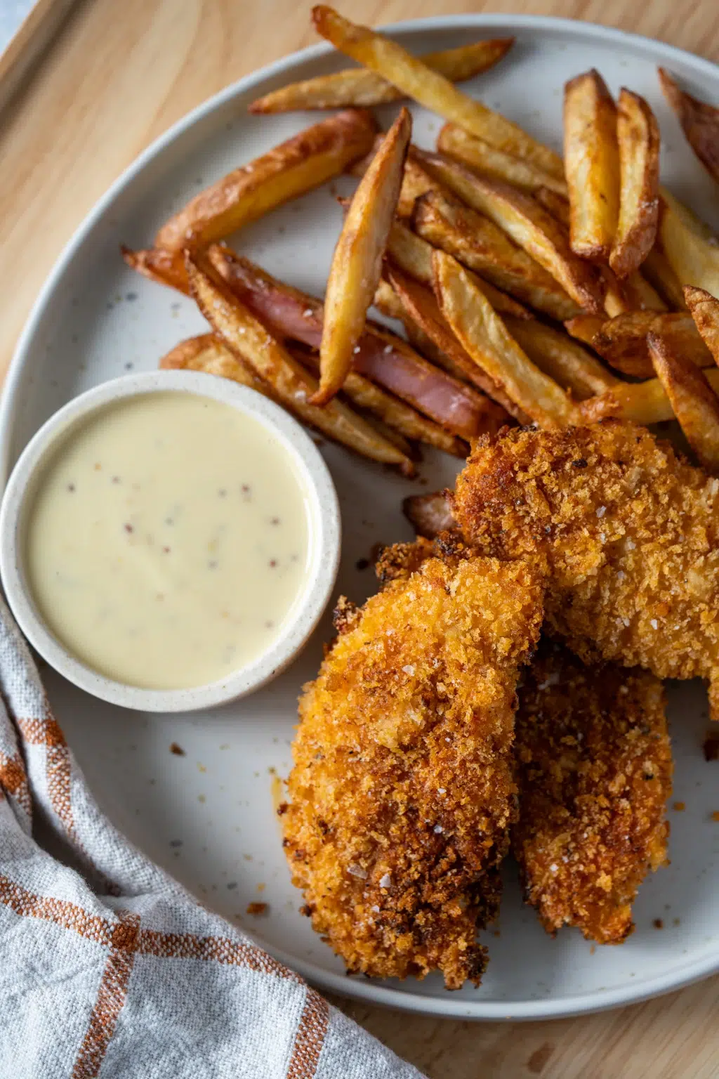 Crispy baked chicken tenders served with fries and mustard dipping sauce on a plate.