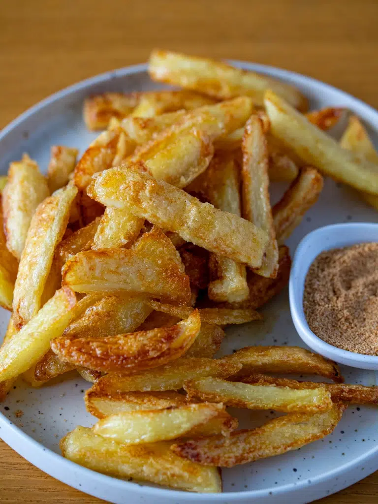 Crispy oven fries served with a side of chicken salt on a white plate