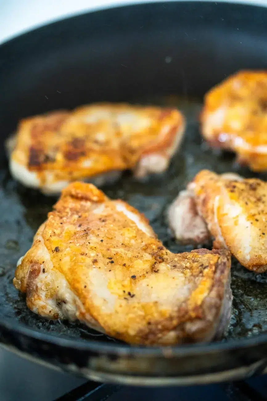Golden brown crispy chicken thighs sizzling in a pan for honey garlic chicken recipe.