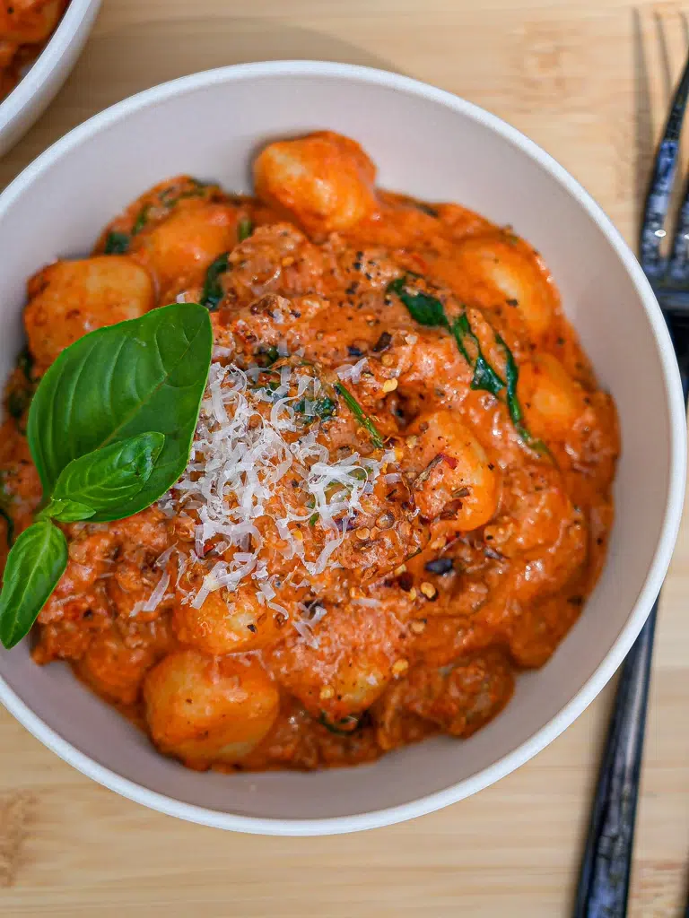 Creamy sausage gnocchi in a bowl, topped with herbs
