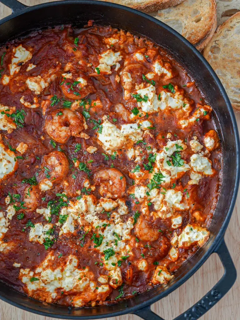 Overhead shot of prawn saganaki in a skillet, garnished with feta cheese and fresh parsley.