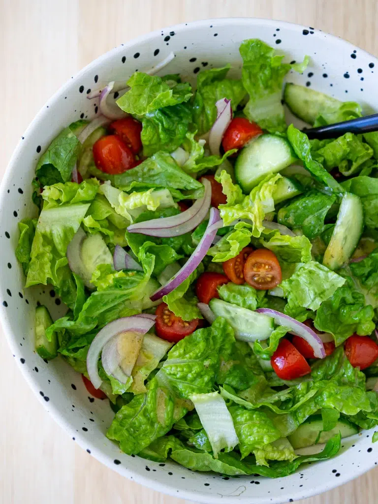 Fresh garden salad with romaine lettuce, cherry tomatoes, red onion, and cucumber in a speckled white bowl.