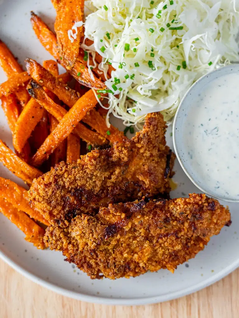 Close-up of Southern 'Fried' Baked Chicken Strips, golden-brown and crispy, served with sweet potato wedges and a side of sour cream for dipping.